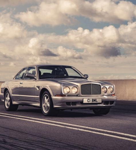The original Bentley Continental GT driving on a road with blue cloudy sky behind