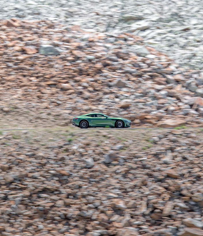 Green Aston Martin DB12 driving on a rocky landscape