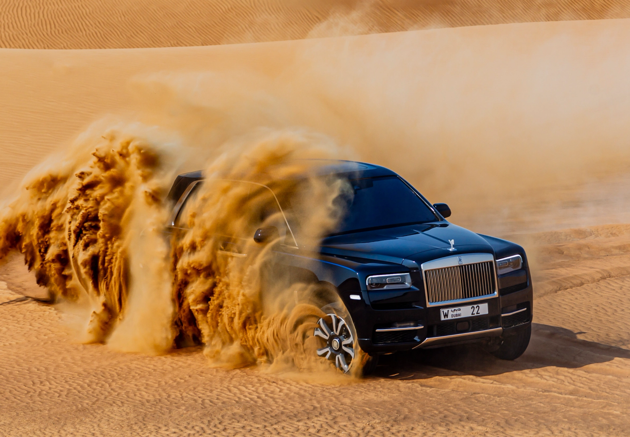 Rolls-Royce Cullinan driving through desert creating sand dust cloud