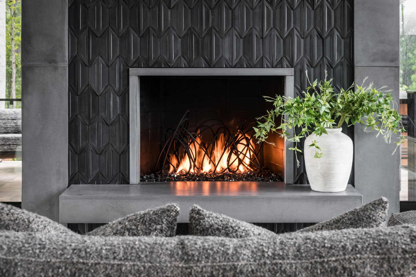 A lit fireplace set into a black tiled surround with a concrete hearth.
