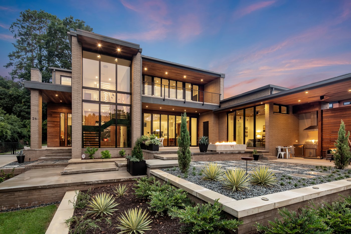 A two-storey home at dusk with large black-framed windows and a landscaped courtyard.