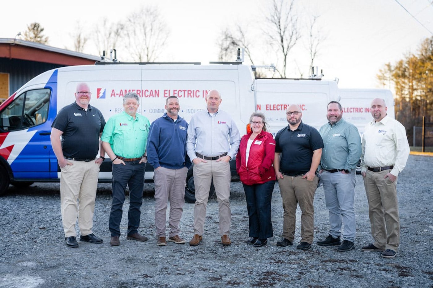 The A-American Electric team standing in front of a company van on a gravel lot.