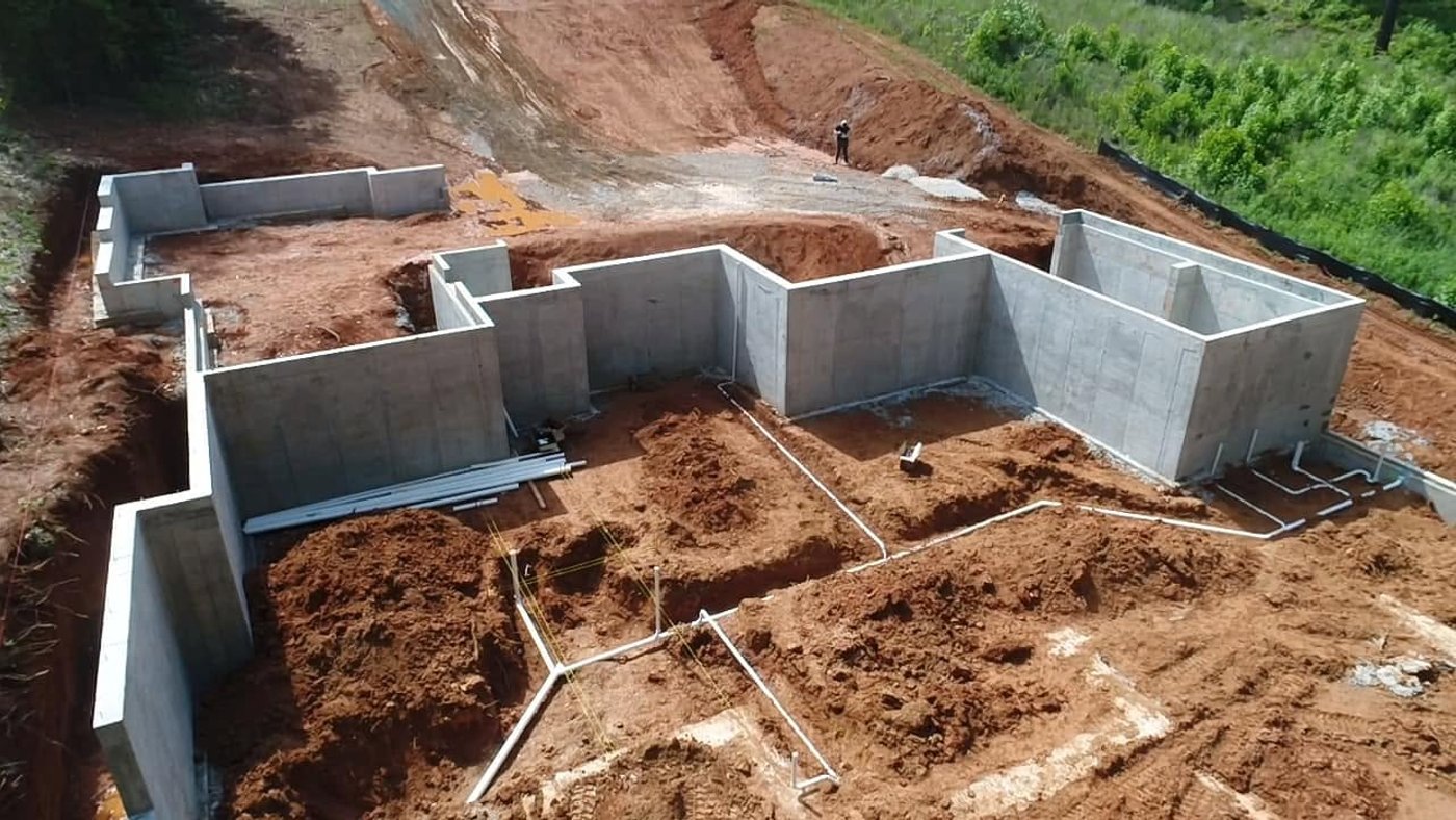 An aerial view of poured concrete foundation walls on a red-clay building site.