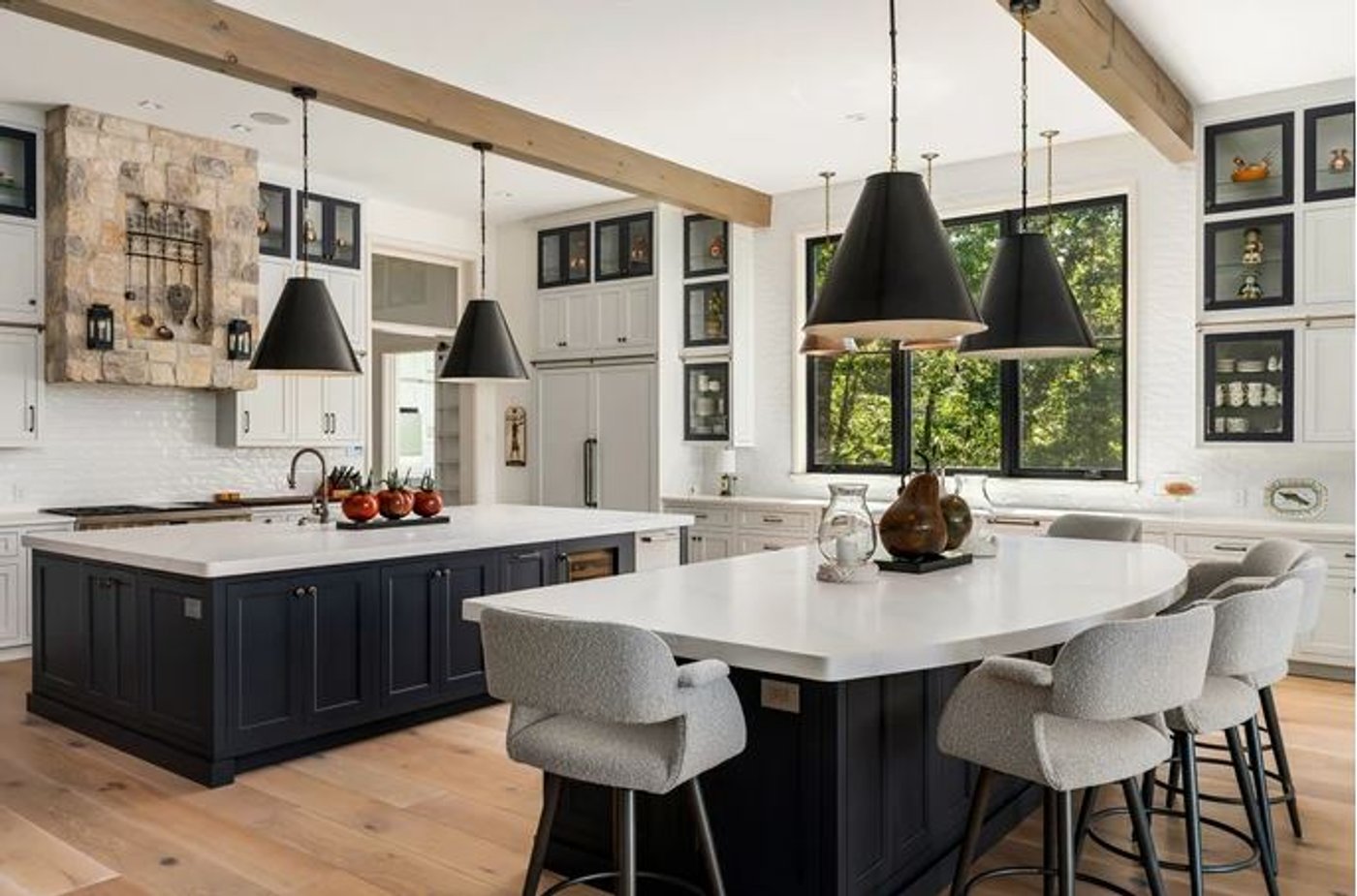 A kitchen with two navy islands, white countertops, black pendant lights and exposed timber beams.