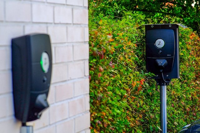 Two Zaptec charging stations: one on a brick wall, the other on a post in front of a hedge.