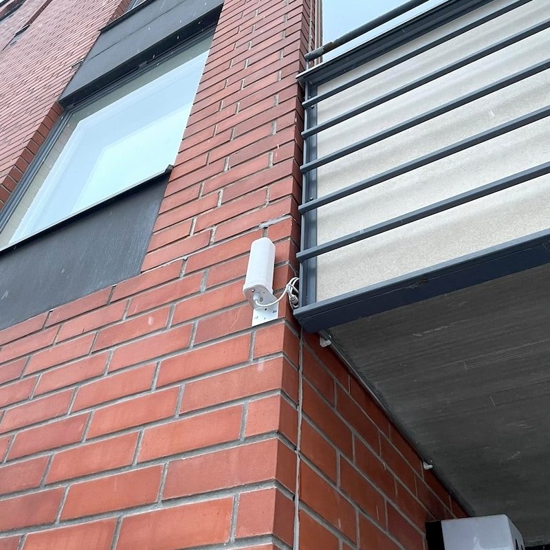 Valkoinen passiiviantenni kiinnitettynä kerrostalon tiiliseinään parvekkeen alapuolelle.