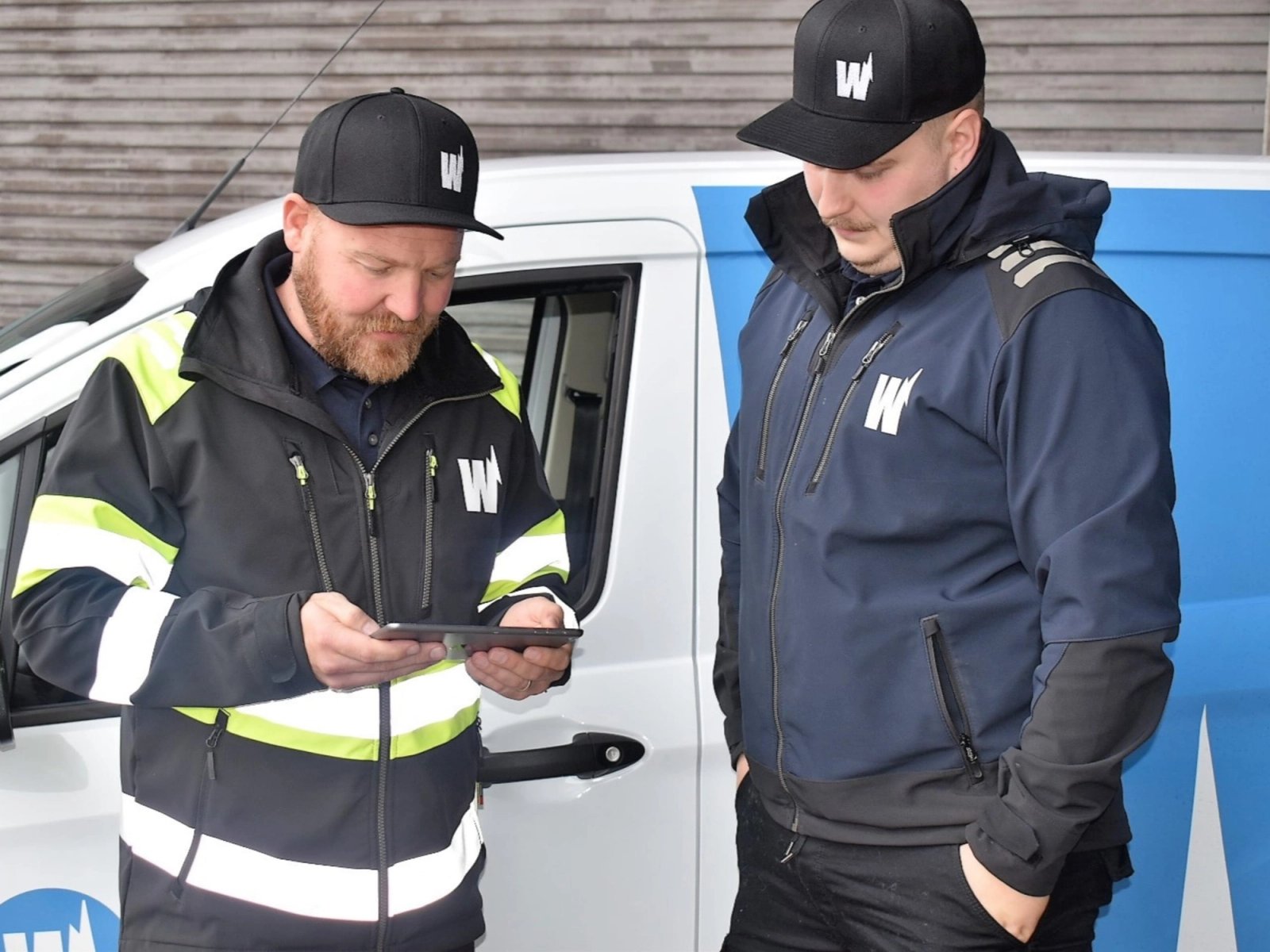 Wirmaxin asentaja näyttää tablettia työkaverilleen pakettiauton vierellä.