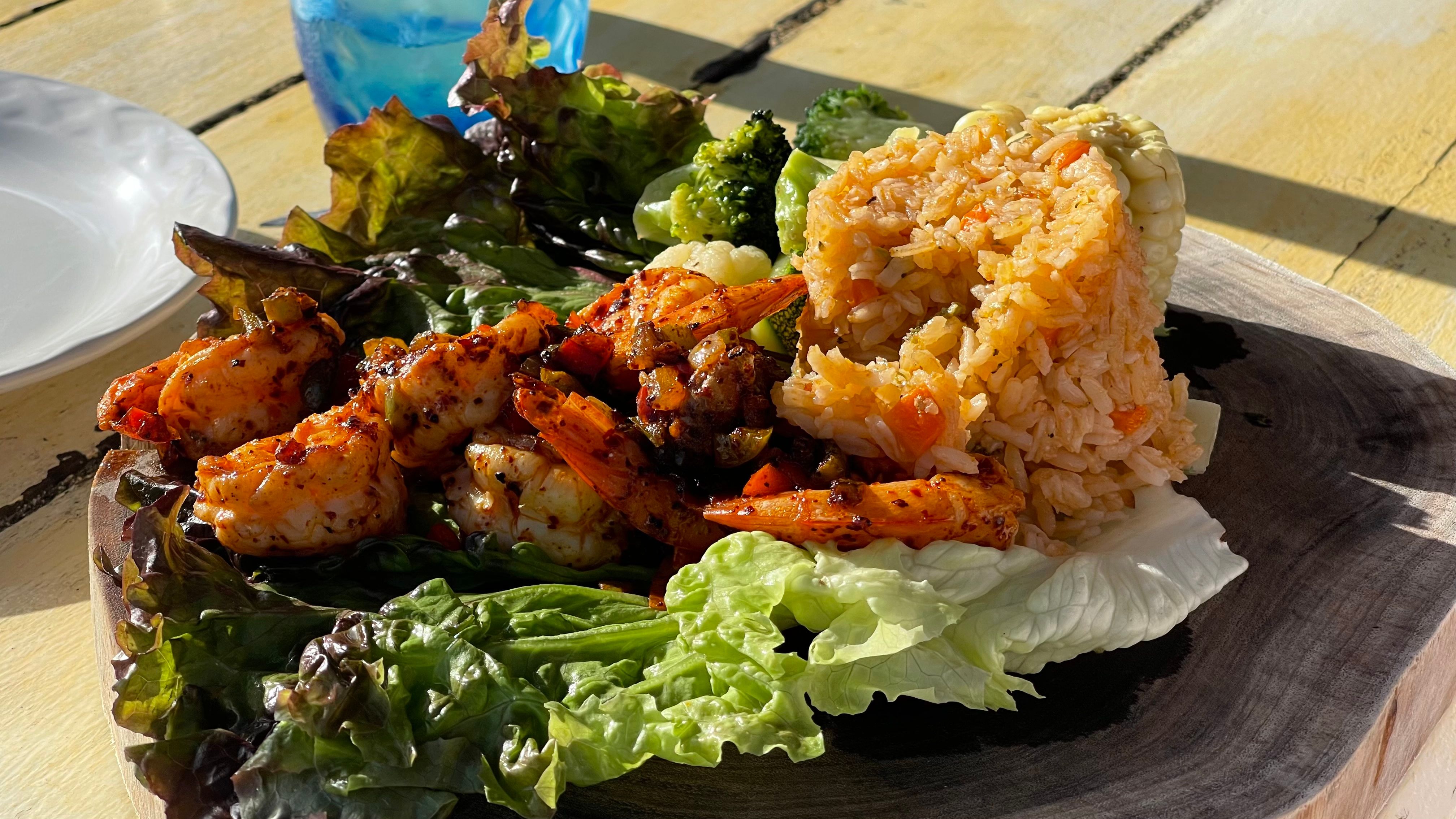 A plated main course with cooked shrimp, rice, vegetables and lettuce leaves