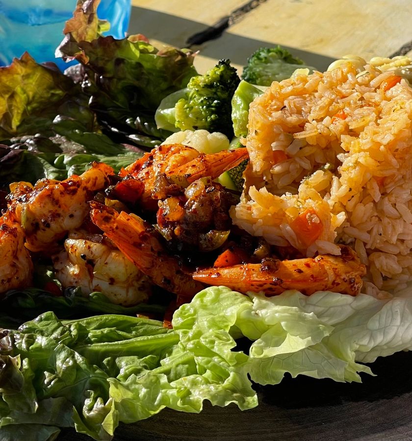 A plated main course with cooked shrimp, rice, vegetables and lettuce leaves