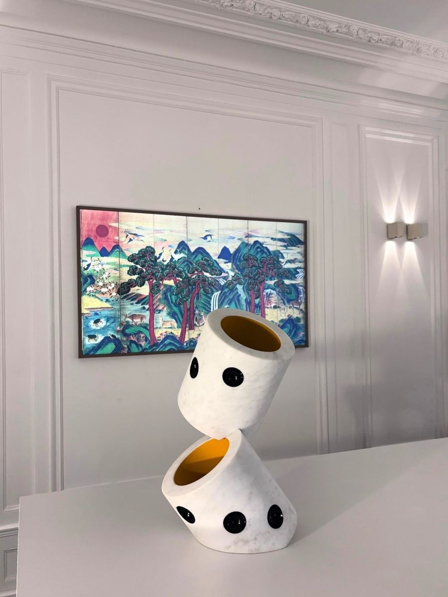 Photo d'une sculpture en céramique blanche à pois noirs et d'un tableau coloré exposés à l'agence PDA, Paris