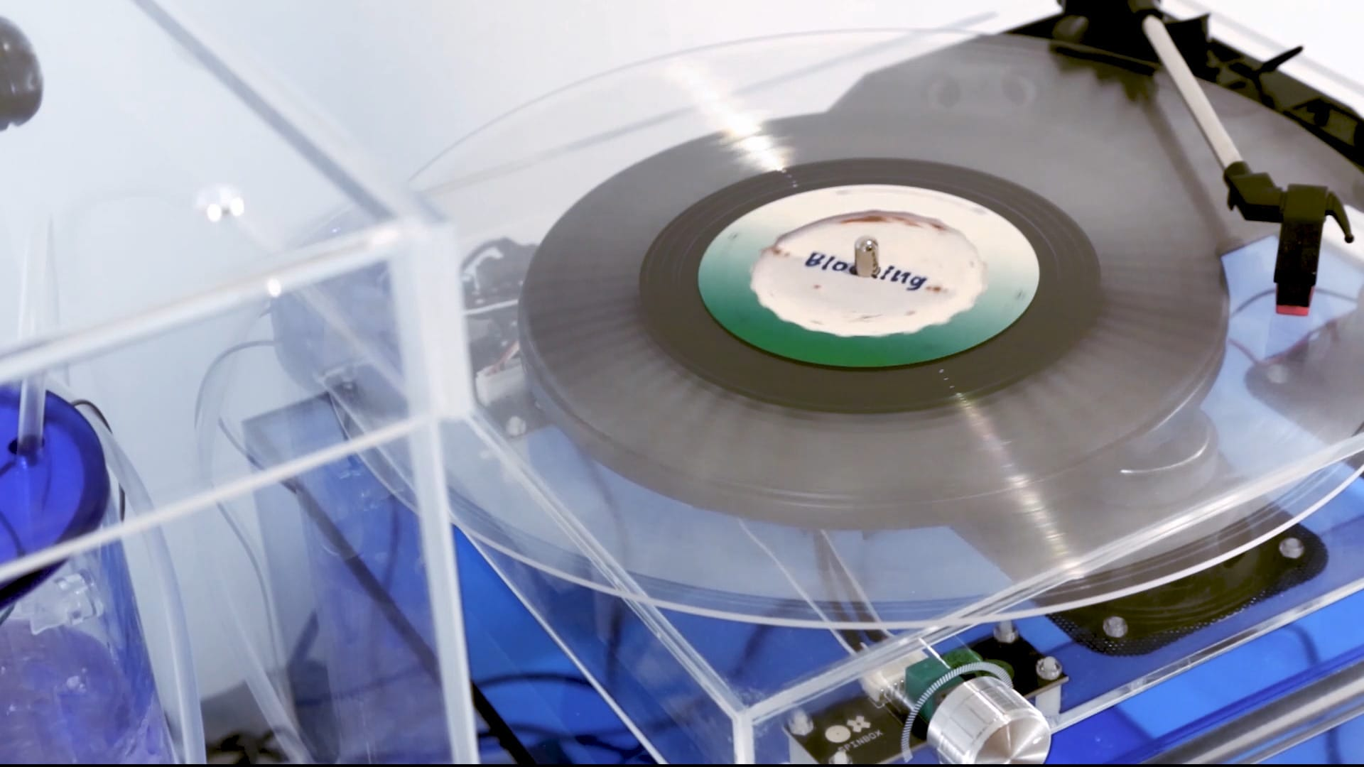 Photograph, taken from above and to the side, of a record player, with a body made from a clear transparent material, playing a transparent record.