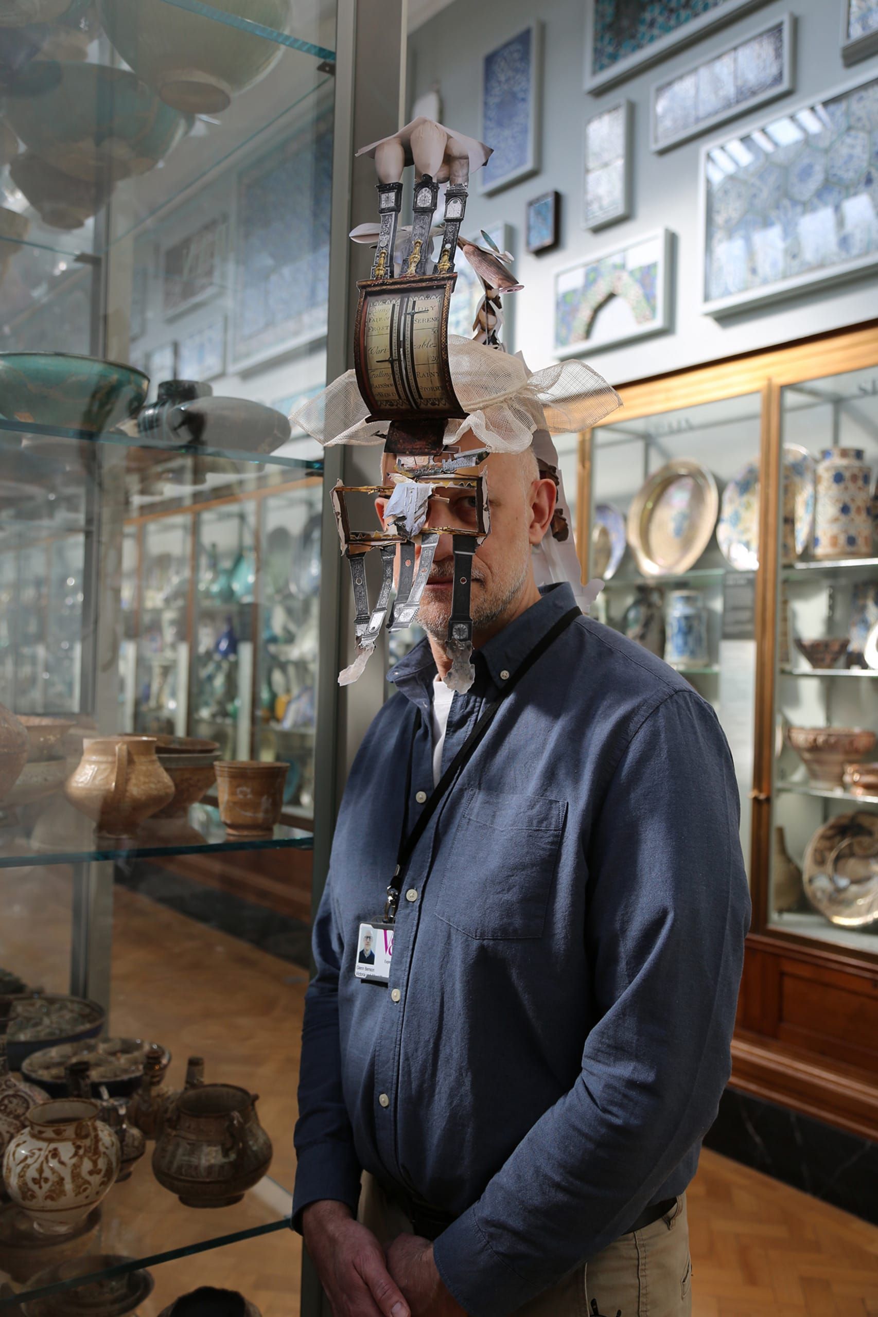 A worker from the V&A stands in one of the museum rooms wearing a headpiece made from a collage of printed images of archival objects.