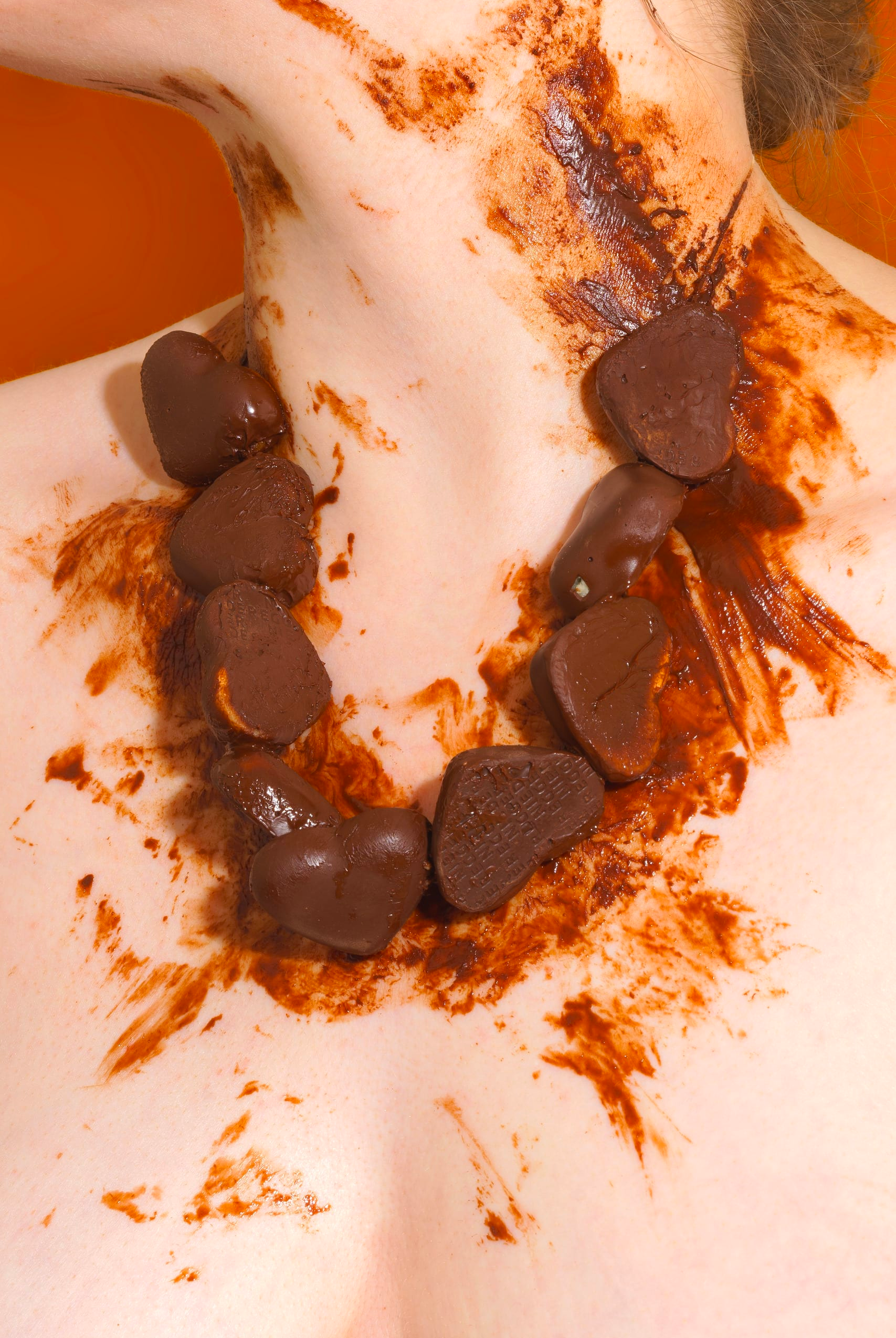 A close-up photograph of a bare neck, wearing a chain of melted chocolates like a necklace, with chocolate smeared over the upper chest and neck, by Francesca Hummler.