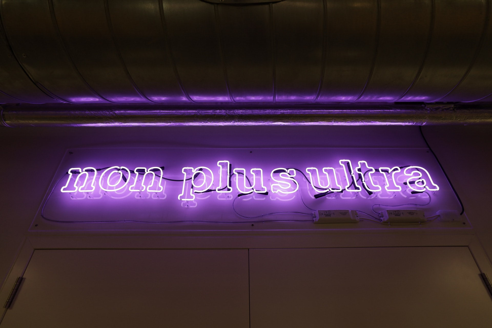 Image of a neon sign in white lettering on a purple background saying ‘Non Plus Ultra’ in an interior location.