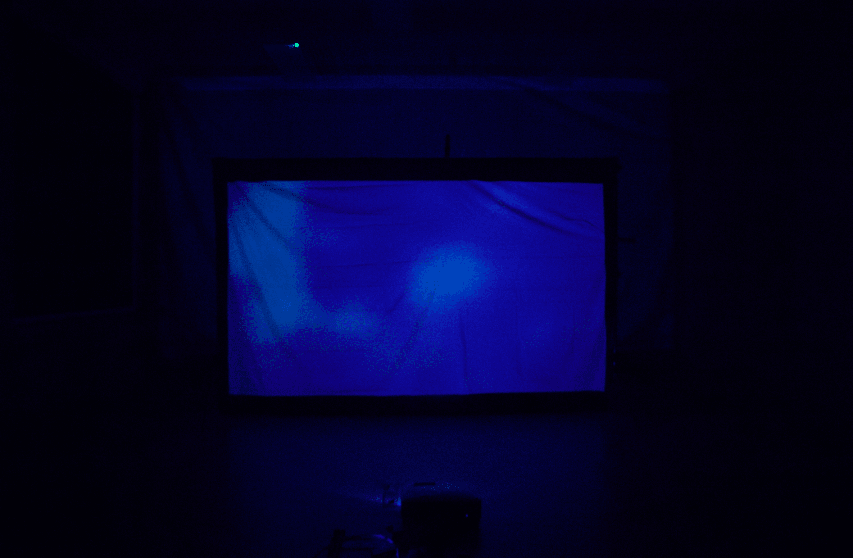 A large rectangular screen or sheet, lit with a blue light, in a very dark space.