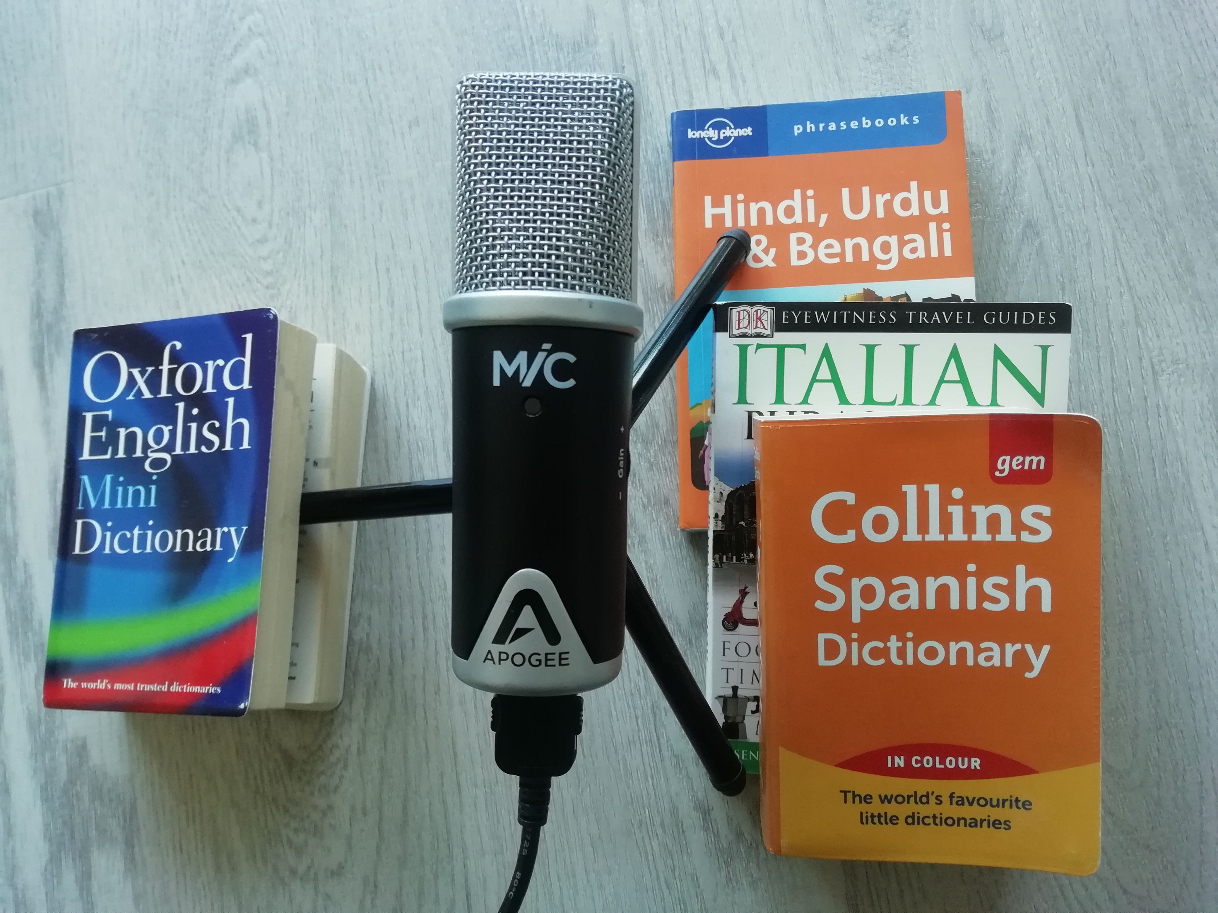 A photograph taken from above of a microphone on a tripod, which stands on various foreign language dictionaries.