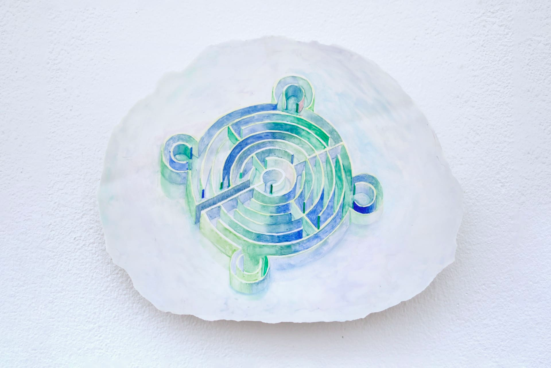 Image of a blue and green circular maze-like object, inside what looks like a round white dish or bowl, with a jagged edge, on a white textured background.