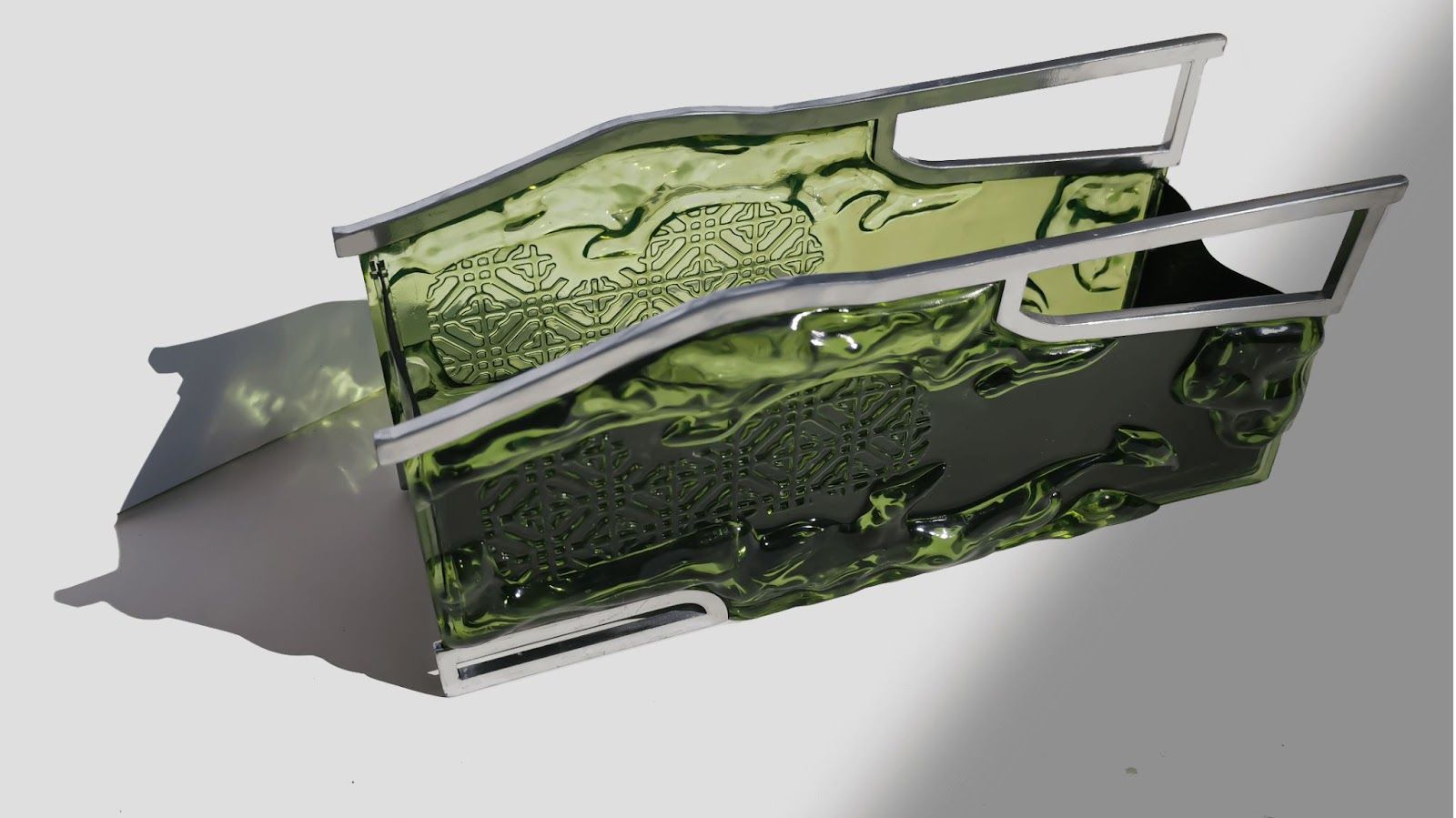 A photograph of a rectangular clutch-style handbag from an angle up above, made in translucent bottle green, embossed resin, with angular chrome handles.