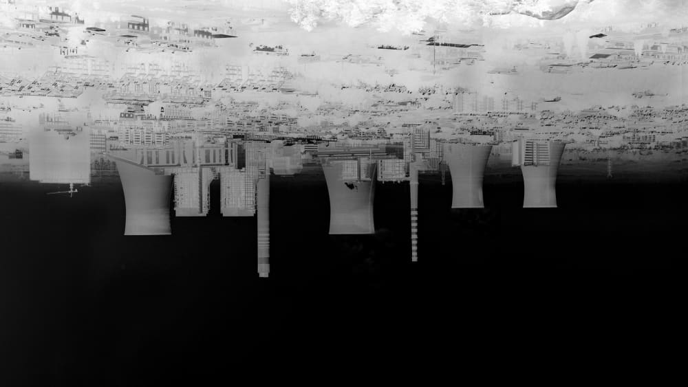 Image that appears to be a black and white photograph or negative orientated upside down, of a power station, set against a black sky at the bottom of the image. 