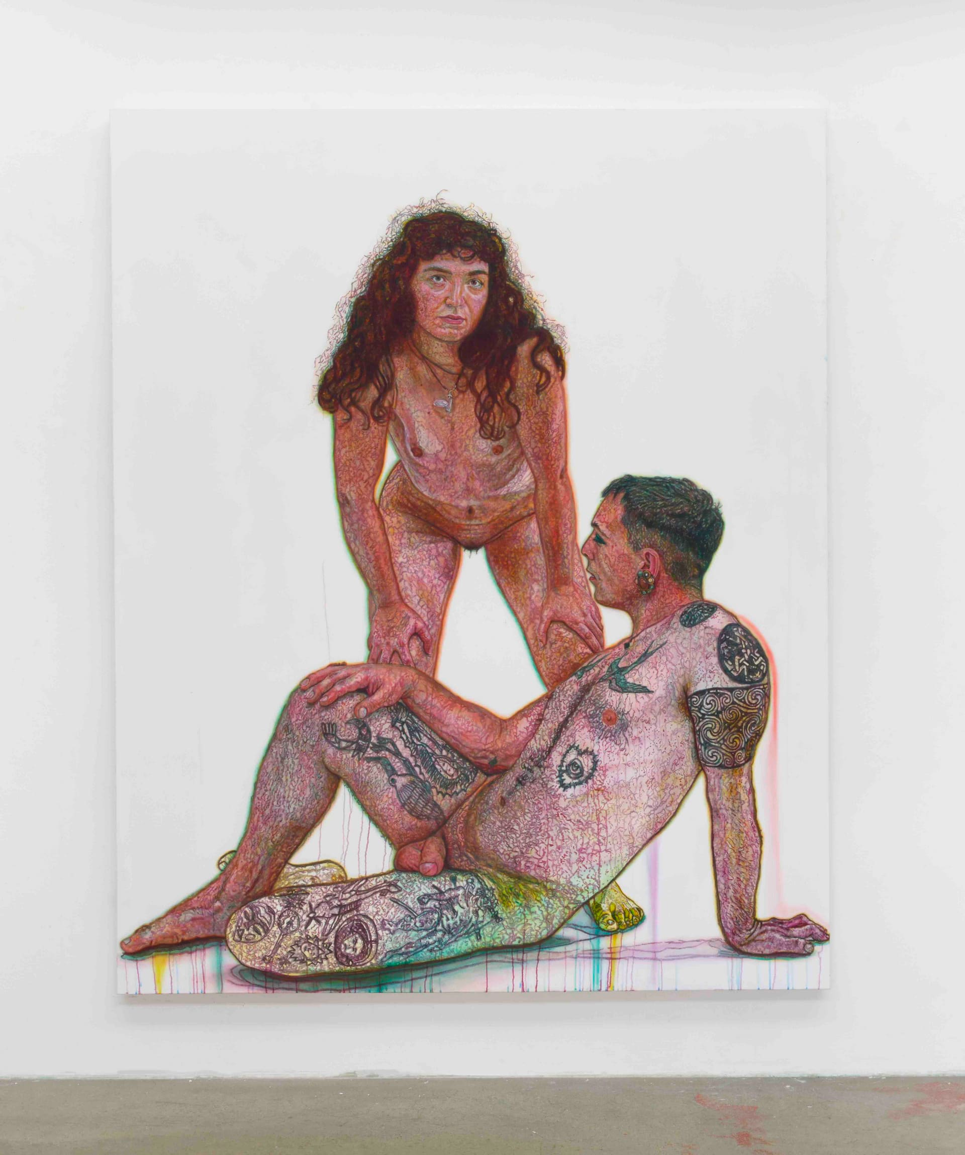 Image of a nude woman leaning forward with her hands on her thighs, looking straight forward, standing above a nude tattooed male, sat in profile, leaning on one arm behind him.