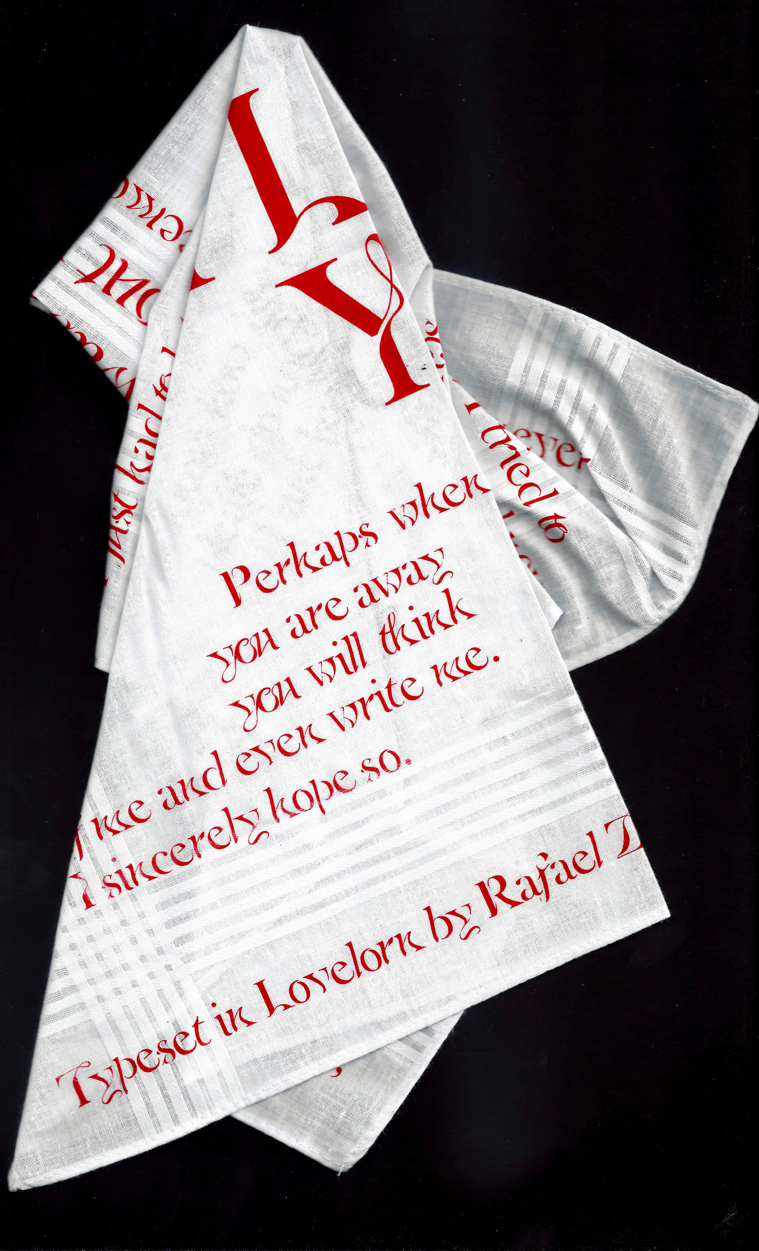 Photograph of a white cotton handkerchief covered in writing in a red font and partially folded, on a black background.