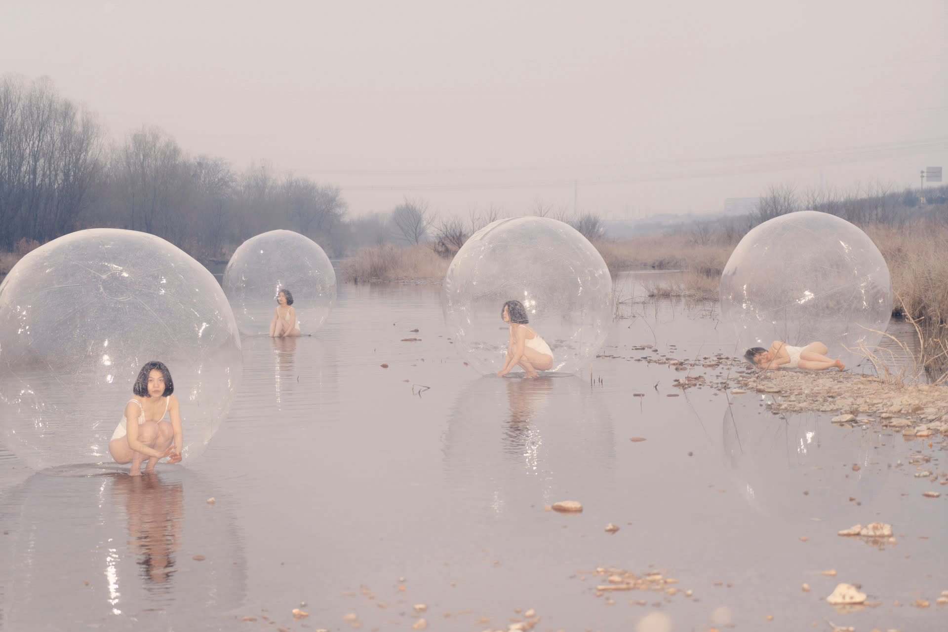 Image of four bubbles, containing a girl in different positions, floating on a river or lake.
