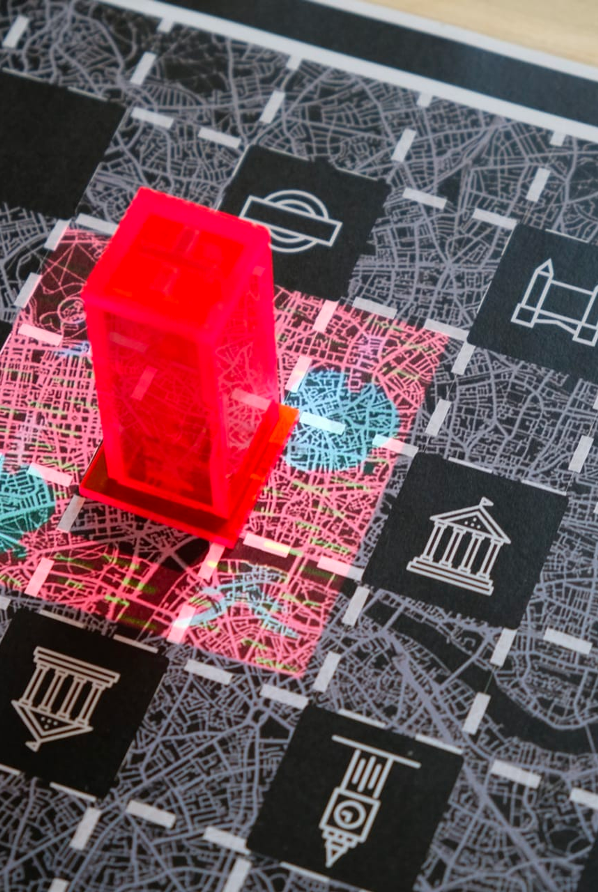 Image of a close-up on what looks like a black, white and red board, with a grid pattern over a street map background, and a red translucent tower shaped object, placed on it. By Zhetong Shen