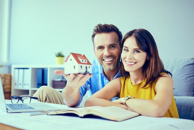 Couple holding house model and reading documents.
