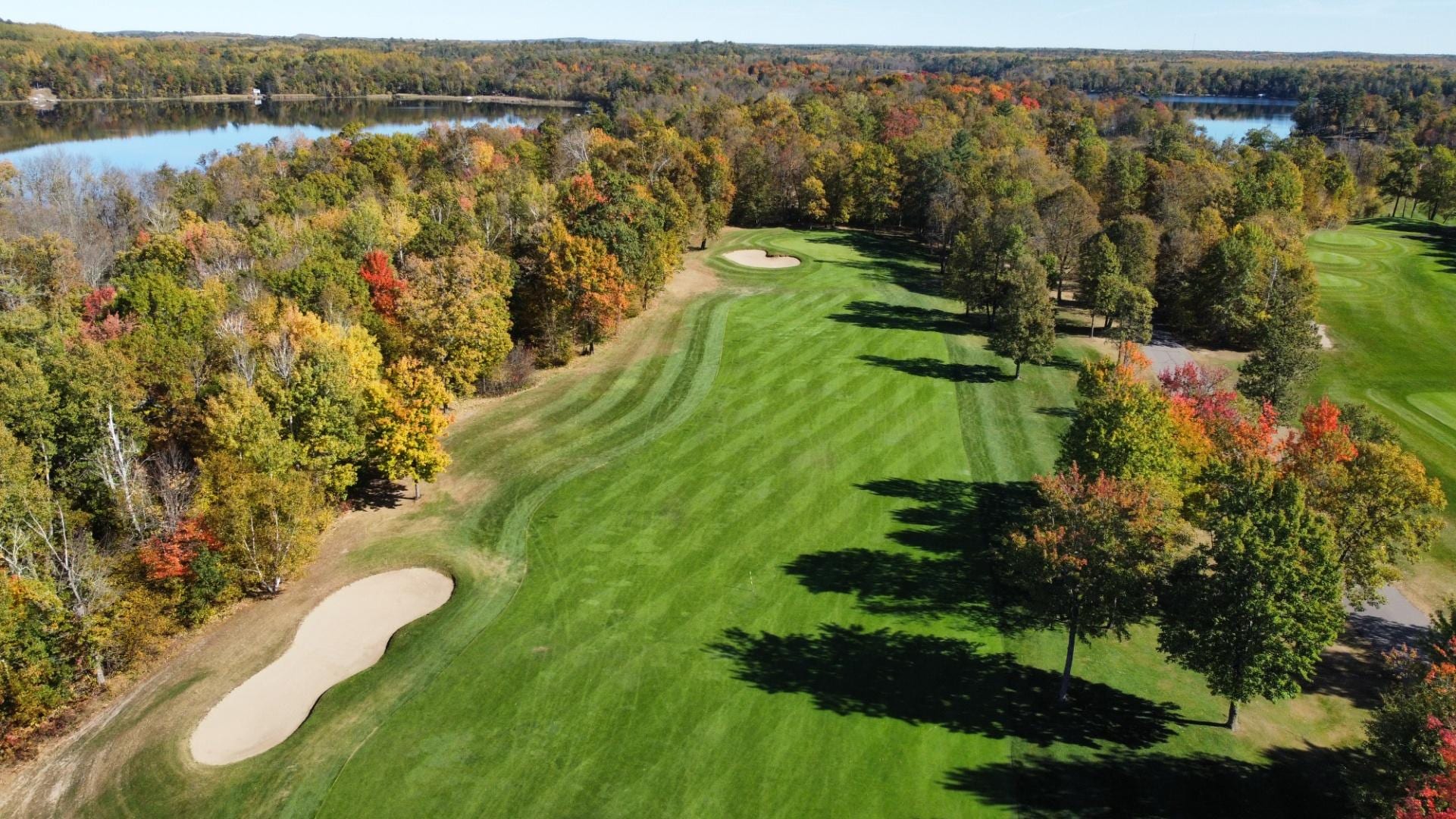 Aerial view of a striped fairway at Golden Eagle lined with fall foliage, with a lake in the background