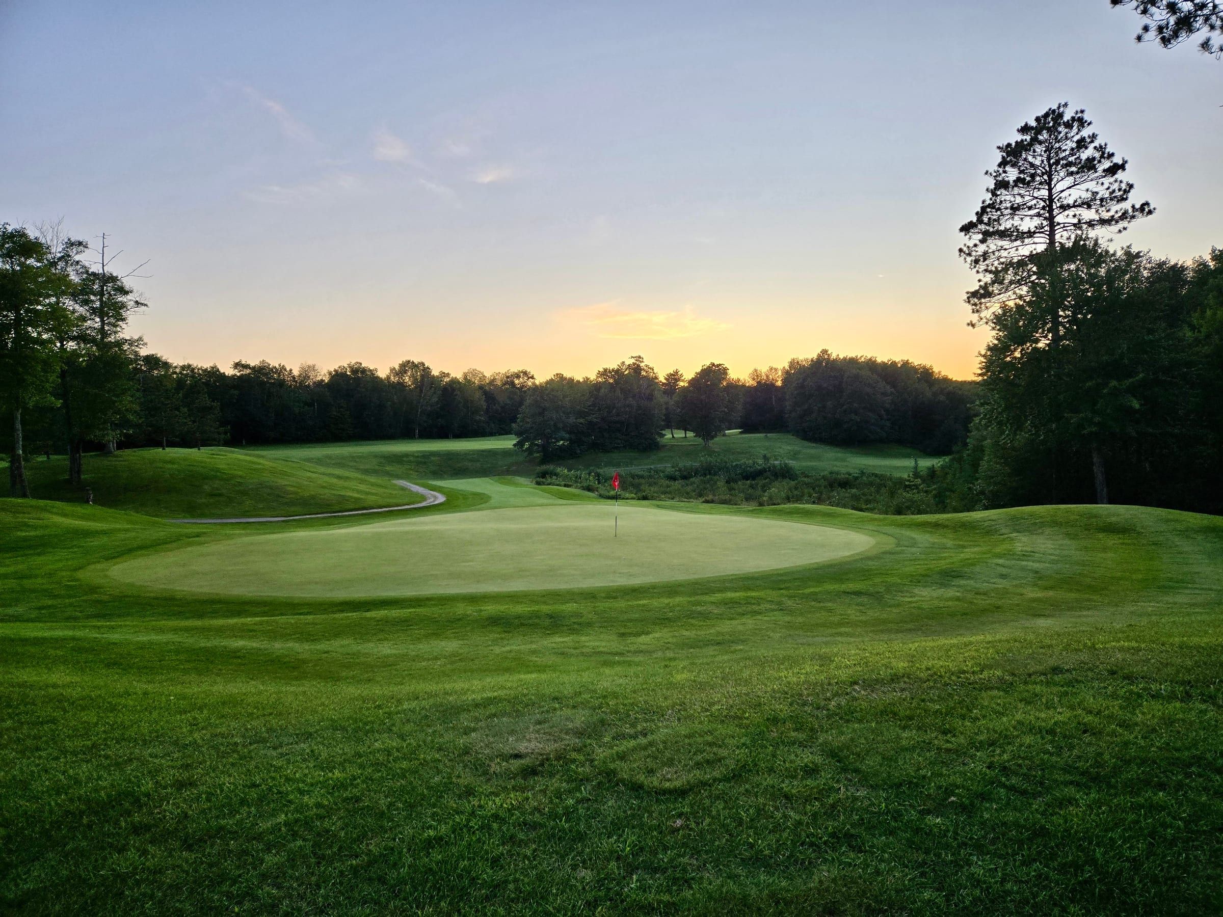 Sunset over a green at Golden Eagle Golf Club with the Northwoods in the distance