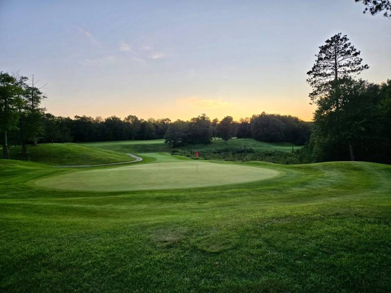 Sunset over a green at Golden Eagle Golf Club with the Northwoods in the distance