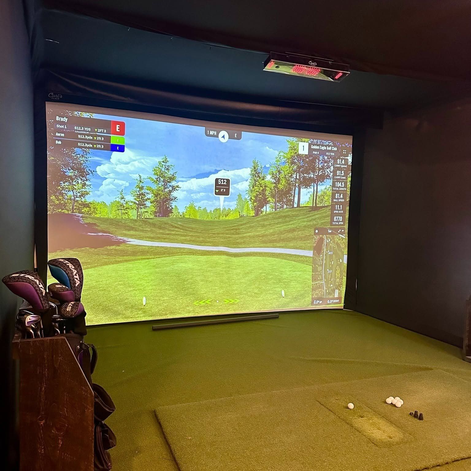 Golden Eagle’s indoor golf simulator bay, with a Golden Eagle hole on the big screen and a bag of clubs on the left