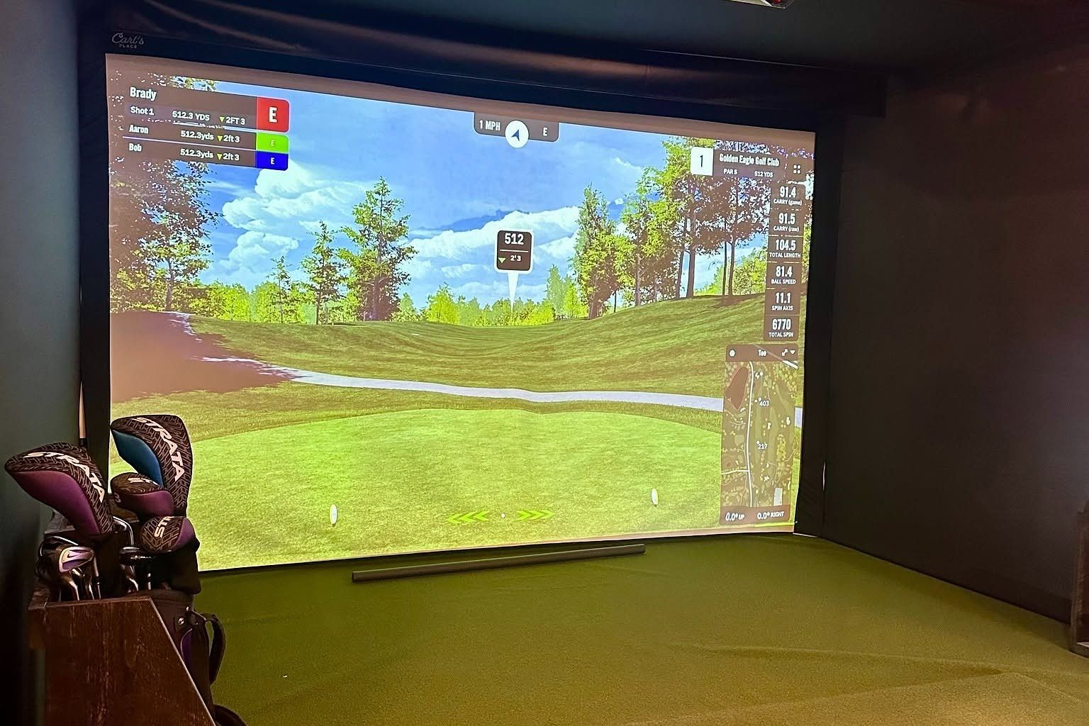 Golden Eagle’s indoor golf simulator bay, with a Golden Eagle hole on the big screen and a bag of clubs on the left
