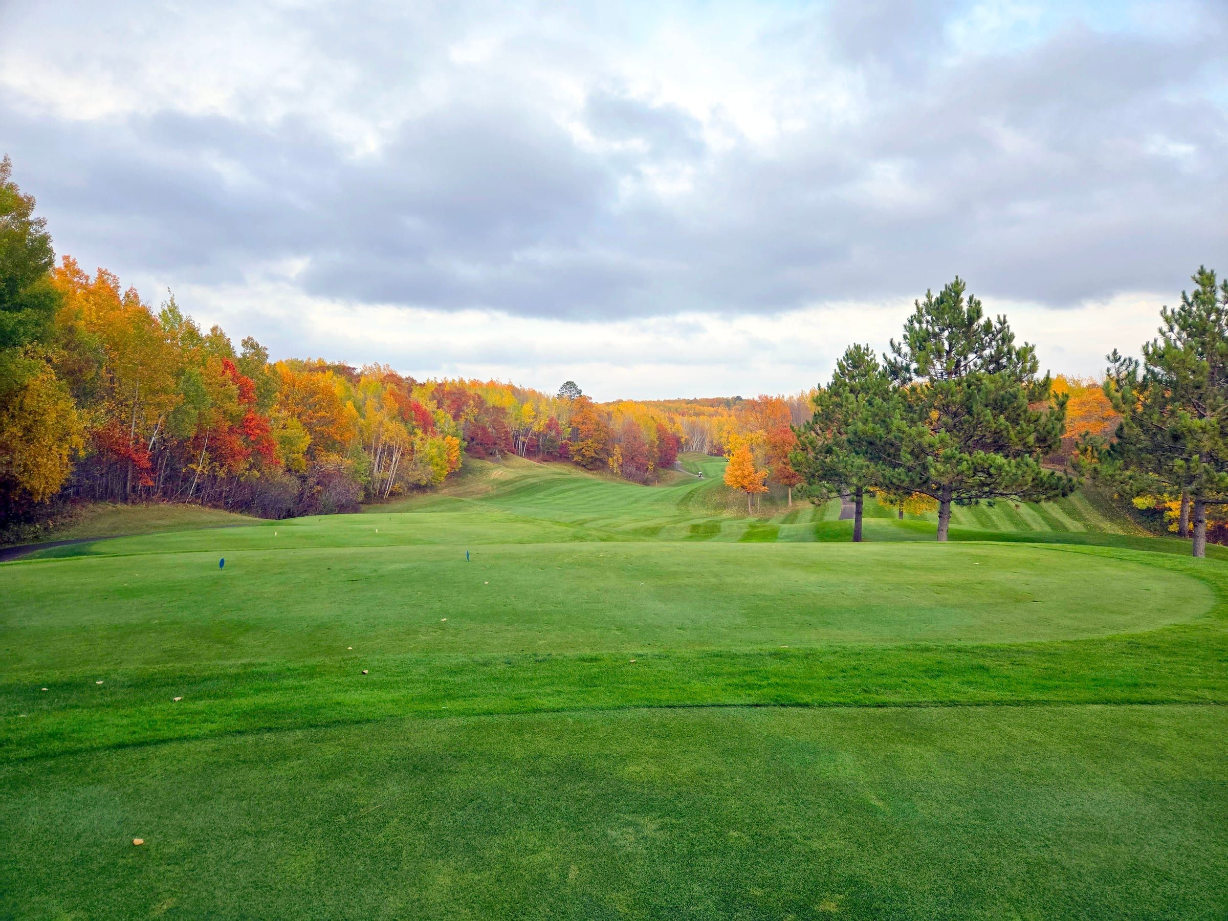 A golfer on the putting green at Golden Eagle, framed by fall-colored trees with a rainbow overhead