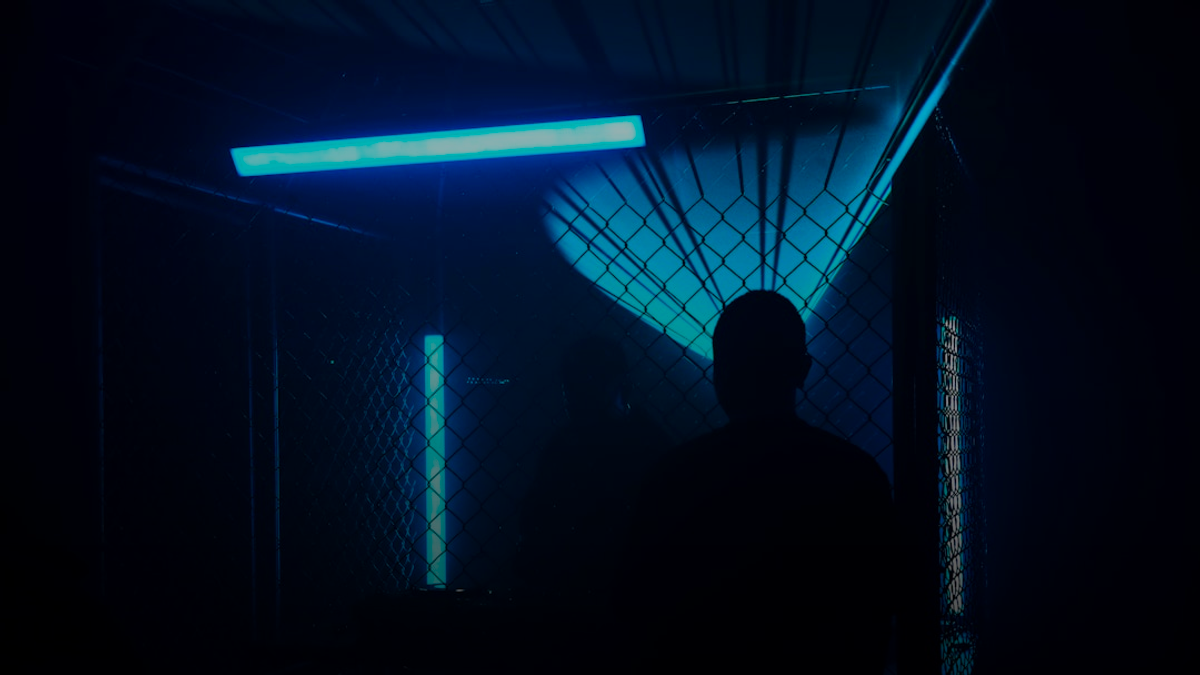 Silhouetted figure in a dark room with blue lights.