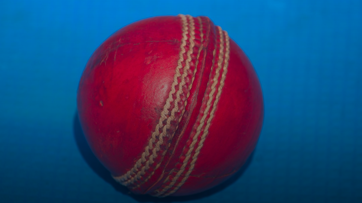 A red cricket ball on a blue surface.