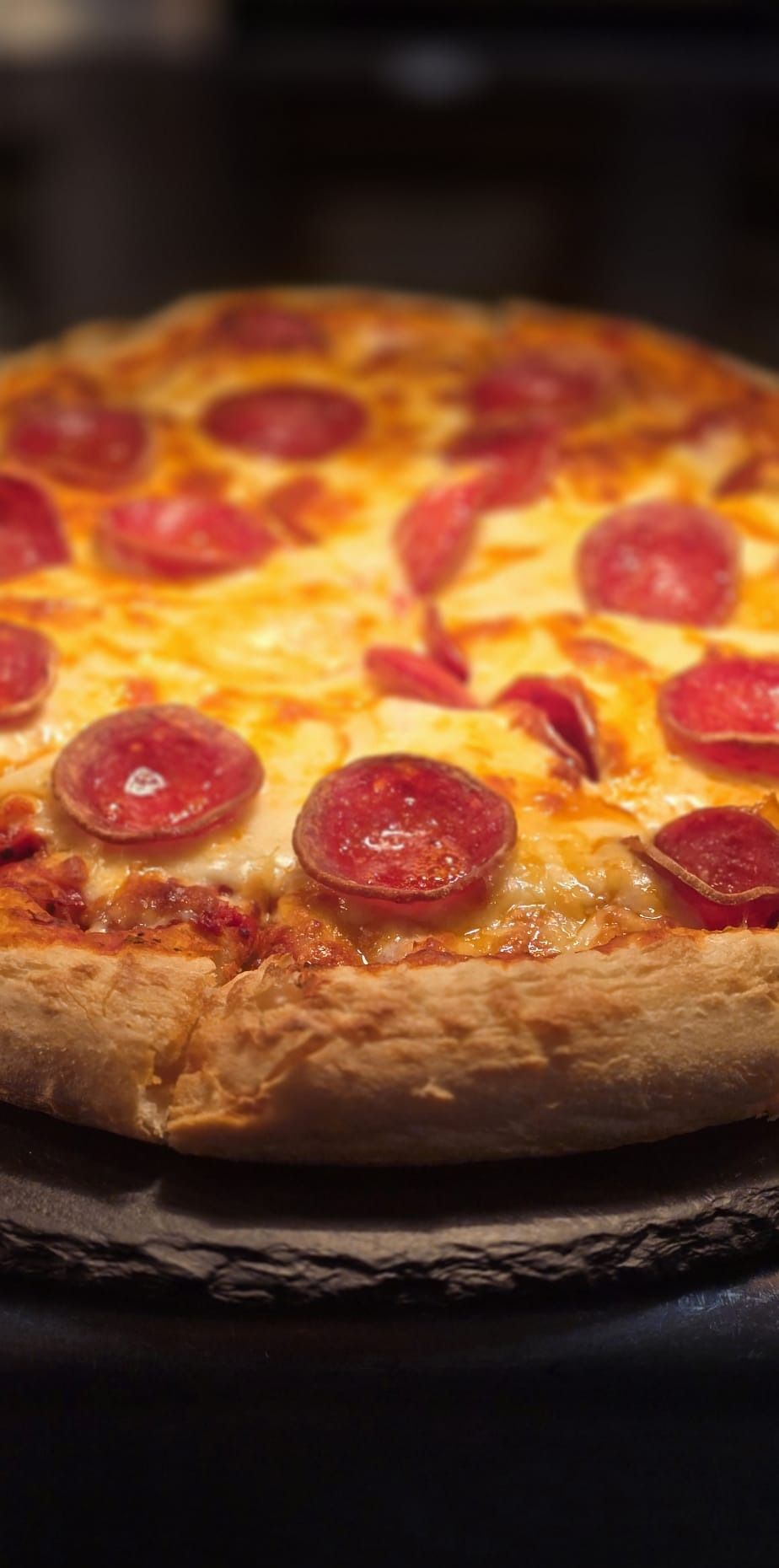 A whole pepperoni pizza on a slate board