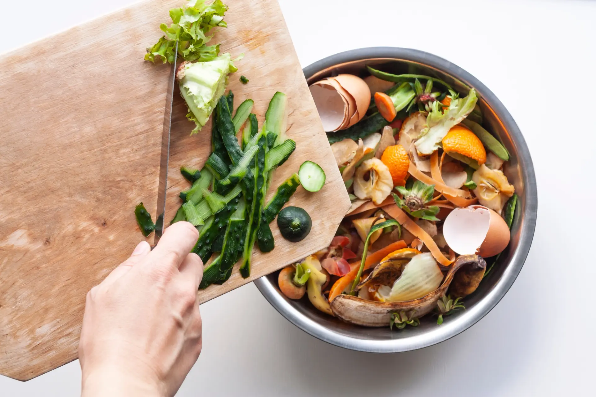 A person carefully slicing vegetables into a bowl with a knife, showcasing an eco-friendly practice to minimize food waste.