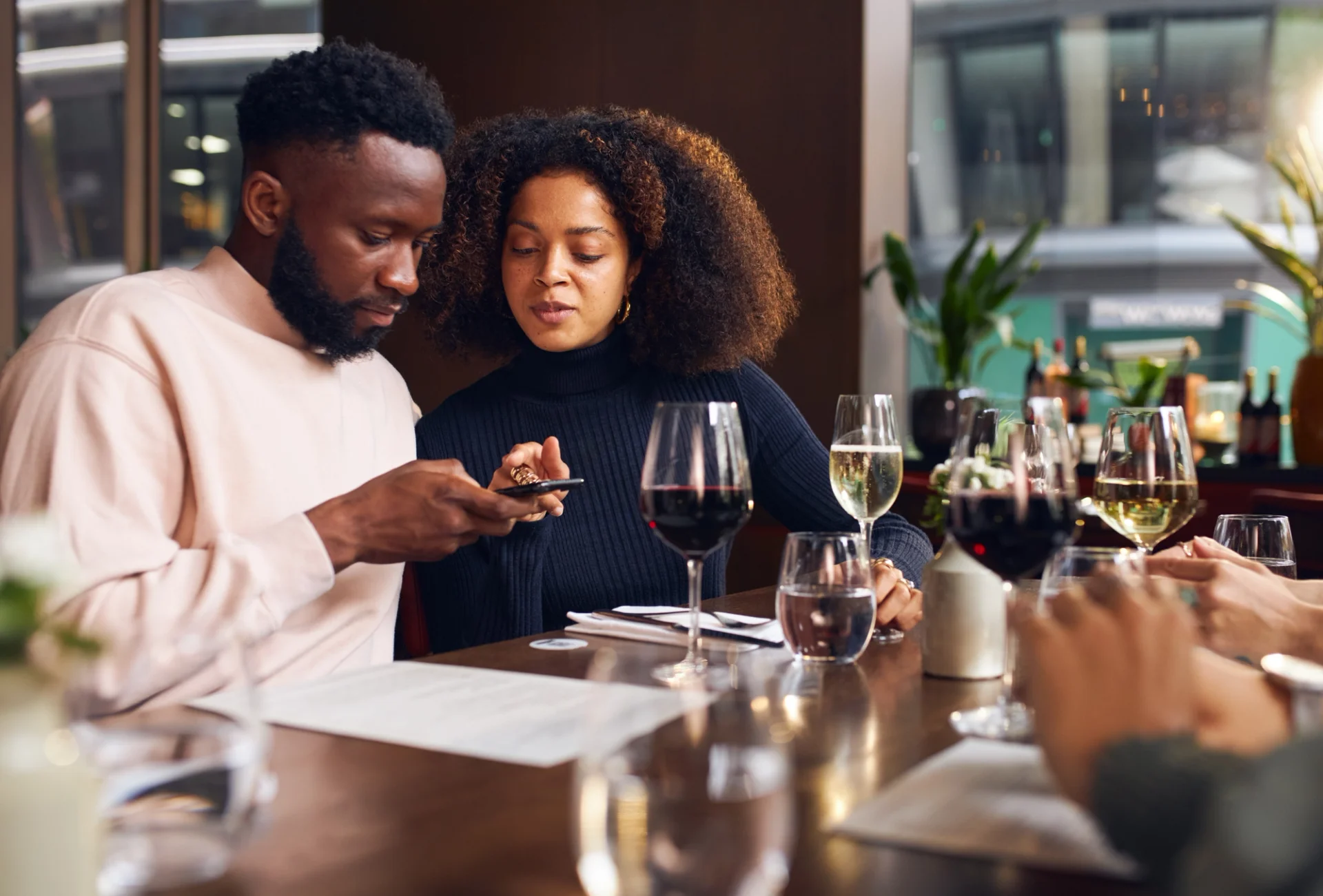 Couple enjoying wine and using phone for QR code ordering at table.
