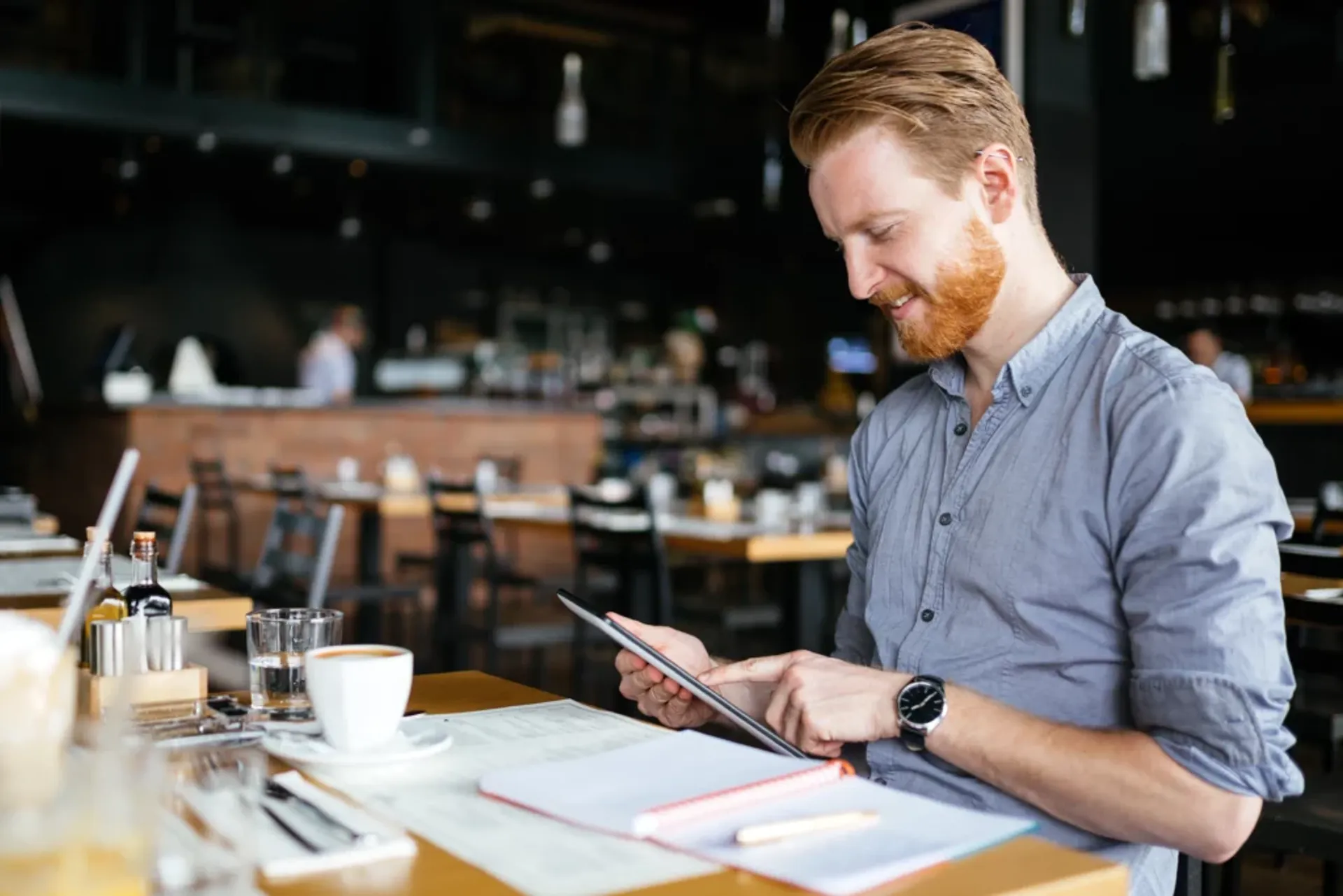 A man seated at a table, engaged with a tablet and arranging restaurant reservations.
