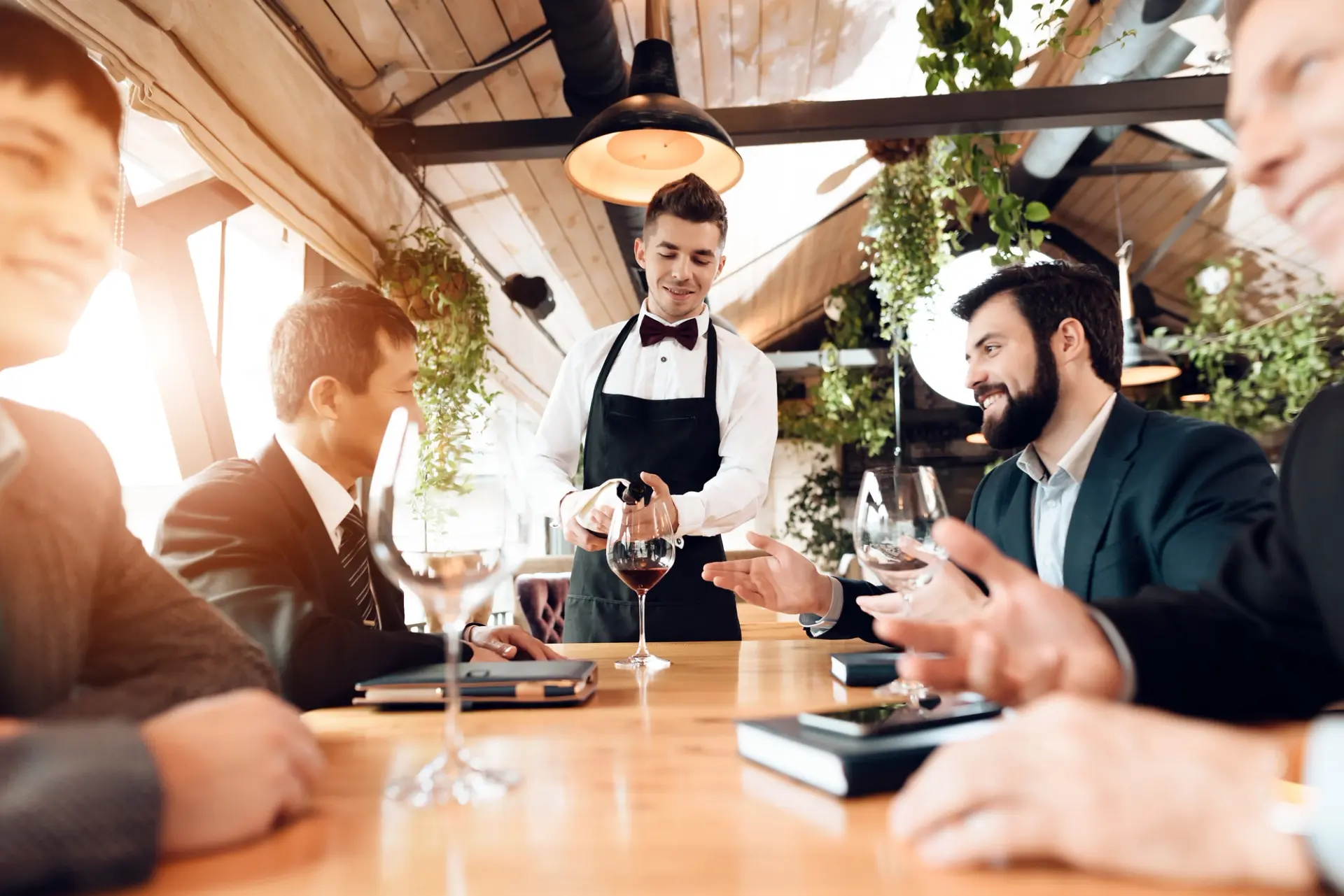 Restaurant waiter pouring wine for coworkers using digital menus in the restaurant.