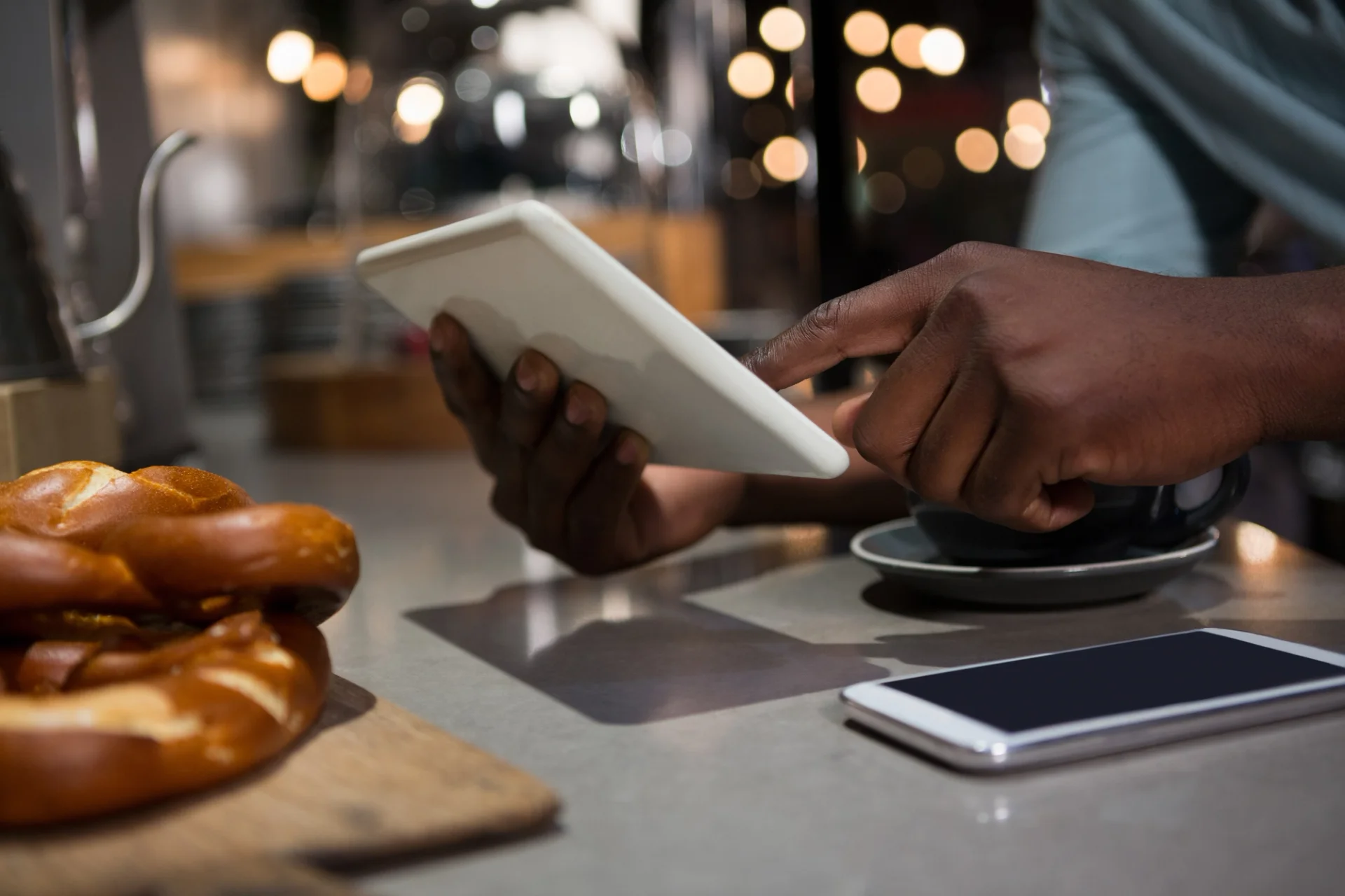 A man engrossed in using a tablet at a coffee shop, exploring the latest restaurant payment trends.
