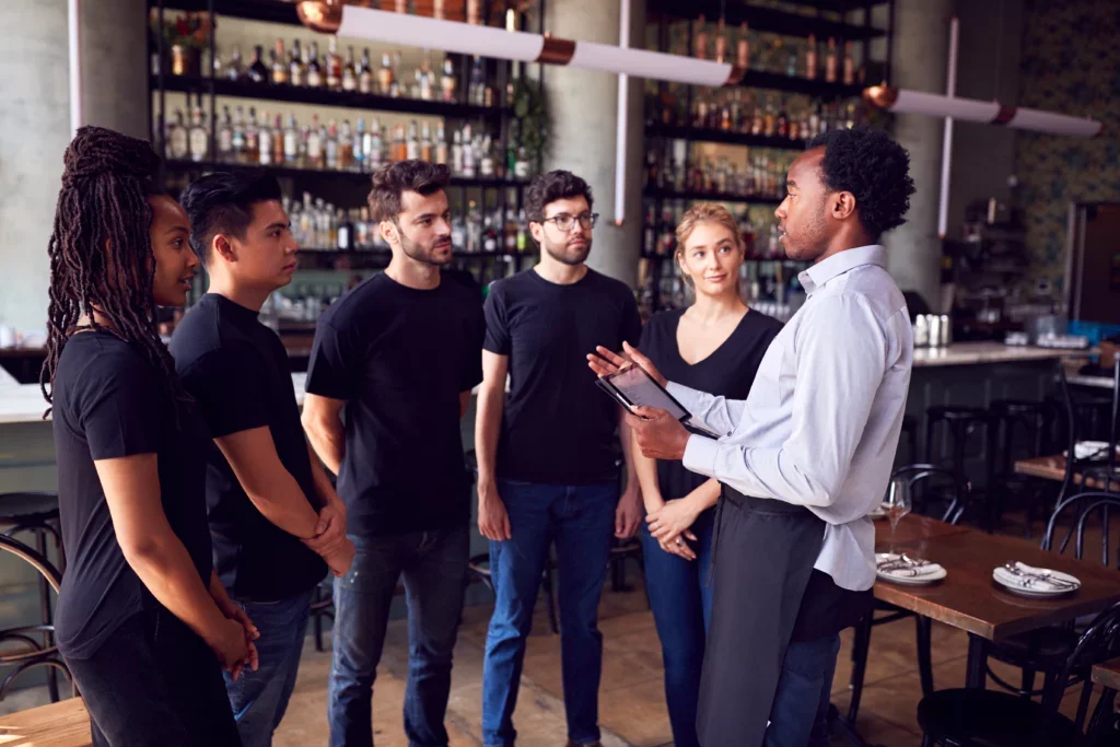 A snapshot of people standing in a restaurant, likely engaged in conversations regarding restaurant management and staff.