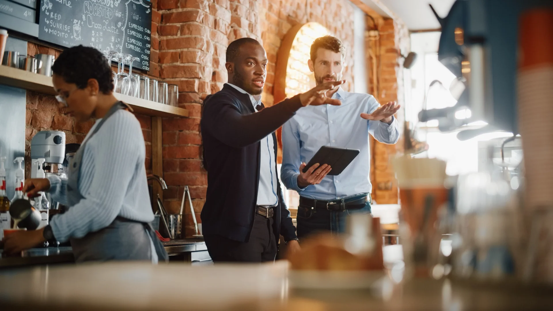Two men using a tablet in a coffee shop, possibly discussing restaurant management tools.