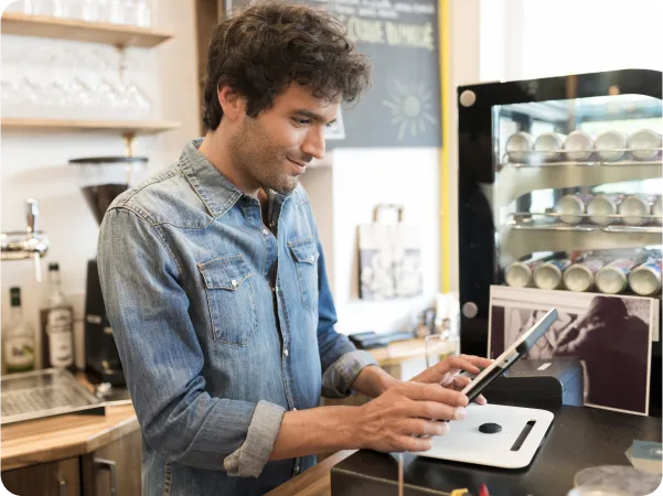 A man in a coffee shop using a tablet to seamlessly send orders from FineDine to Revel.