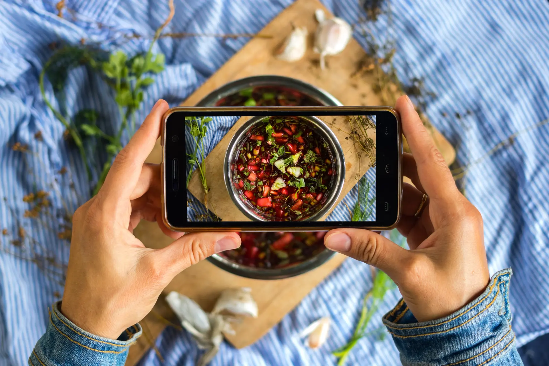 Manos fotografiando un bol de salsa con el móvil desde arriba sobre una mesa preparada