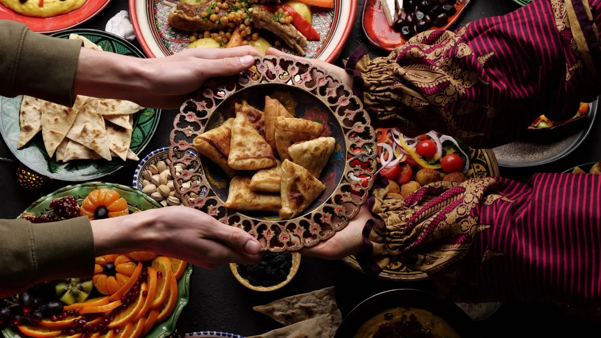 يدان تتشاركان طبق المعجنات وسط مائدة إفطار رمضانية غنية