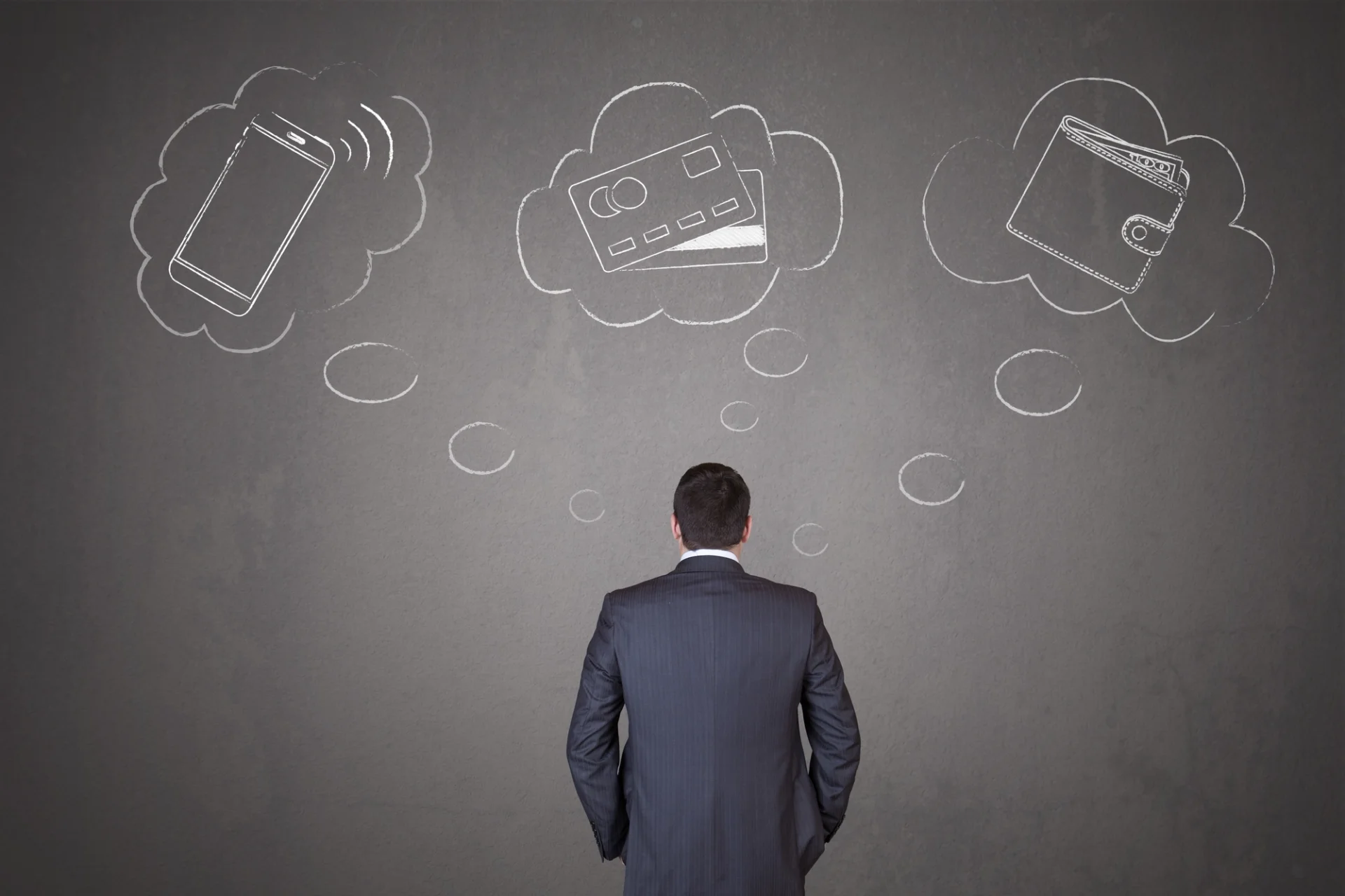 A businessman ponders credit cards and mobile phones, contemplating payment options.