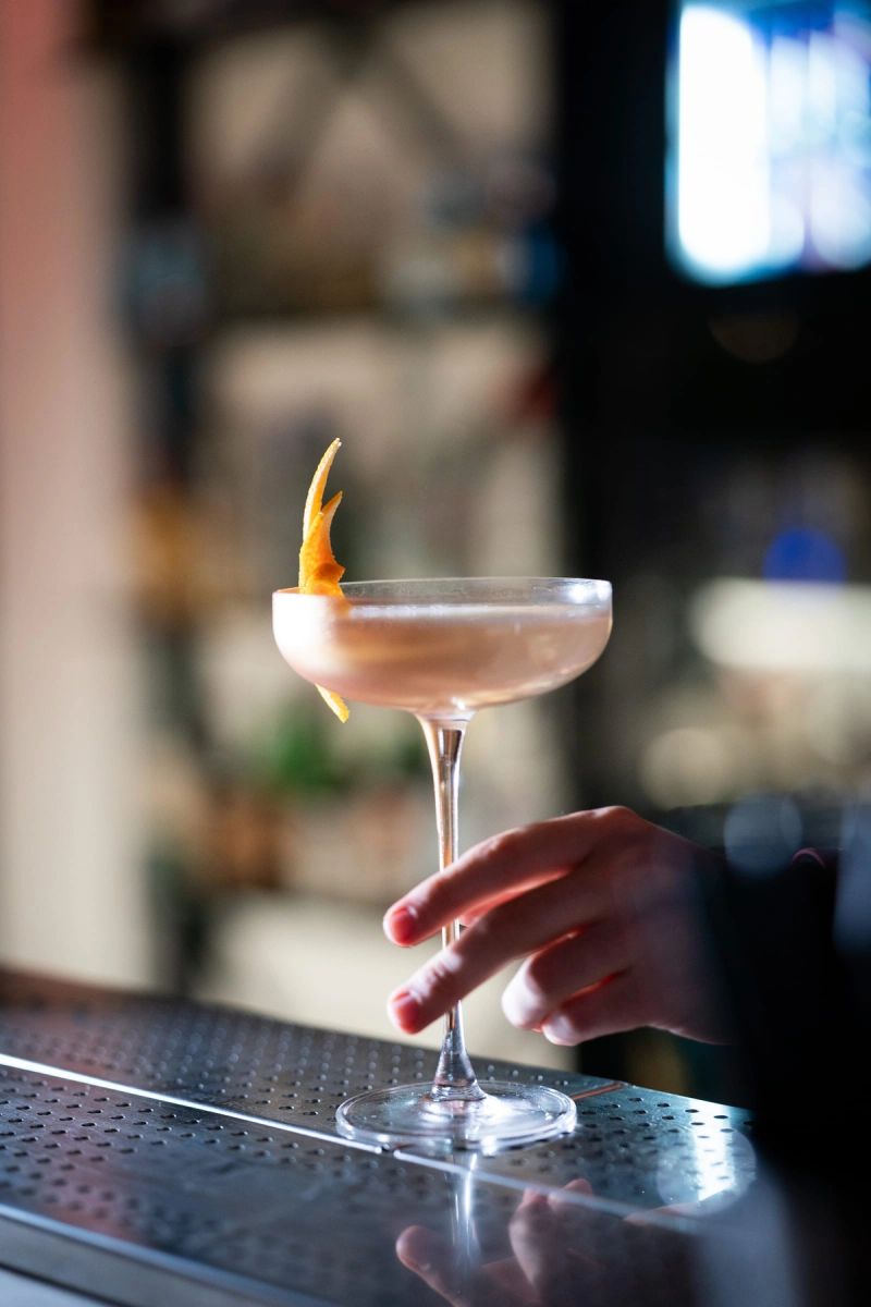 Una mano appoggia una coppa da cocktail sul bancone di un locale