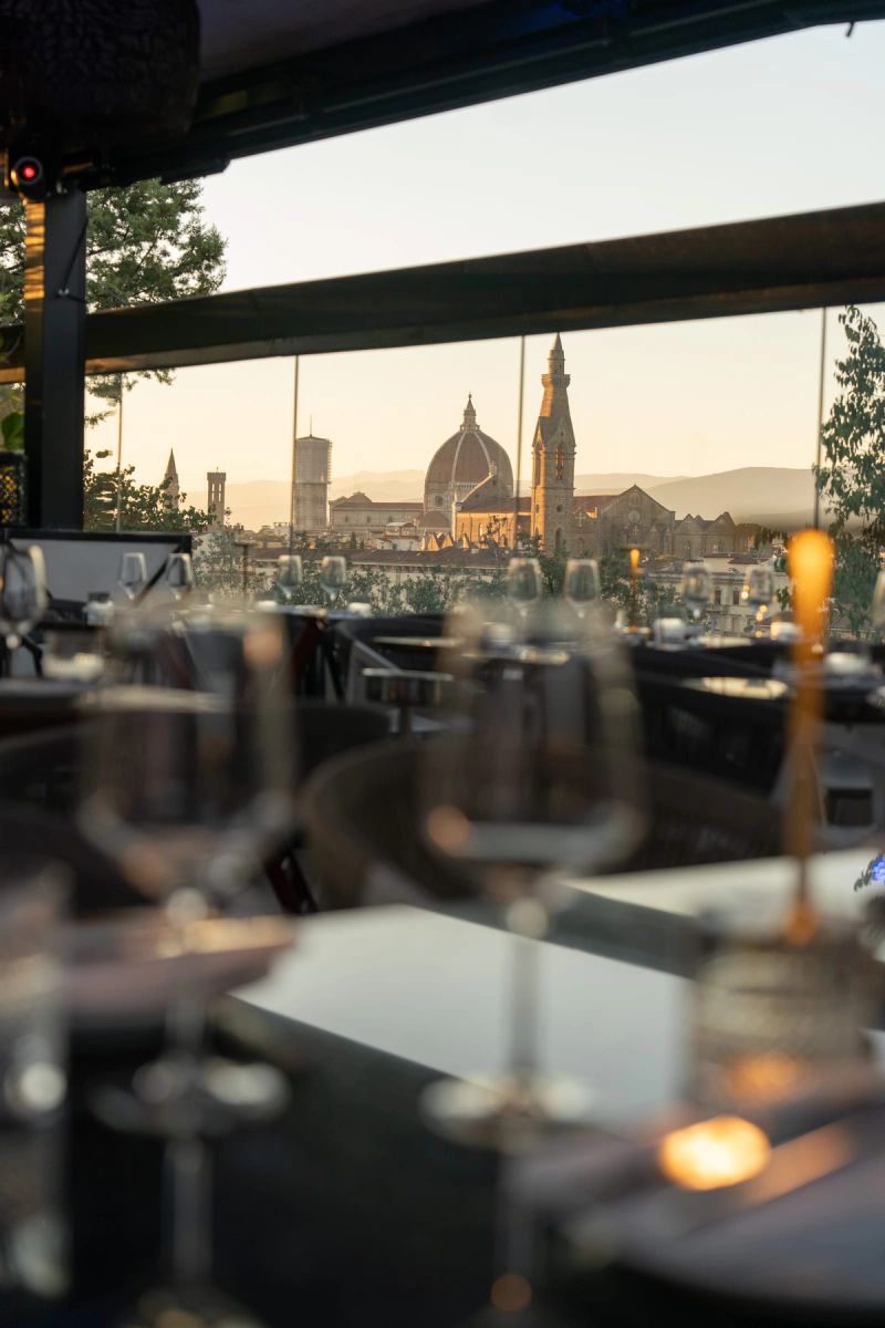 Un tavolo di ristorante apparecchiato, con la cupola del Duomo di Firenze fuori dalla vetrata